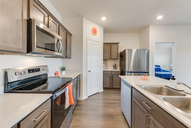 kitchen featuring appliances with stainless steel finishes, wood finished floors, light countertops, a sink, and recessed lighting