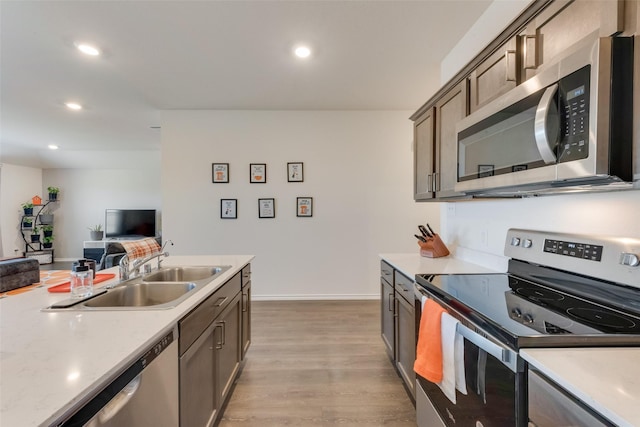 kitchen with open floor plan, stainless steel appliances, light countertops, light wood-style floors, and a sink