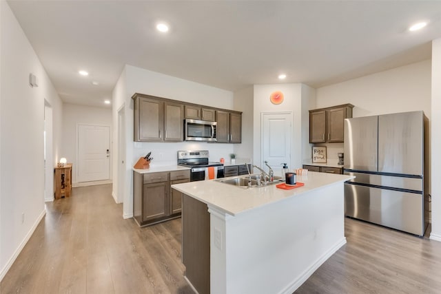 kitchen with stainless steel appliances, an island with sink, sink, and light wood-type flooring