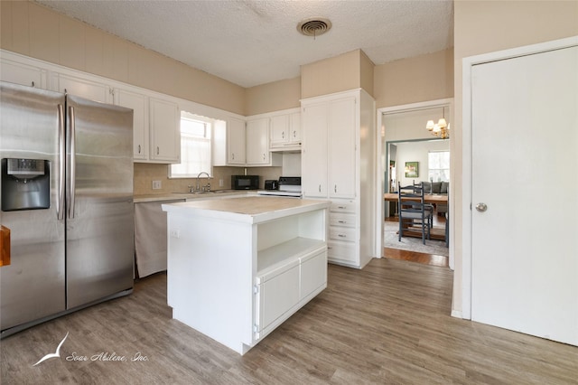 kitchen featuring hardwood / wood-style floors, a center island, white cabinets, a textured ceiling, and stainless steel appliances