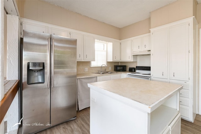 kitchen with appliances with stainless steel finishes, sink, white cabinets, hardwood / wood-style floors, and a kitchen island