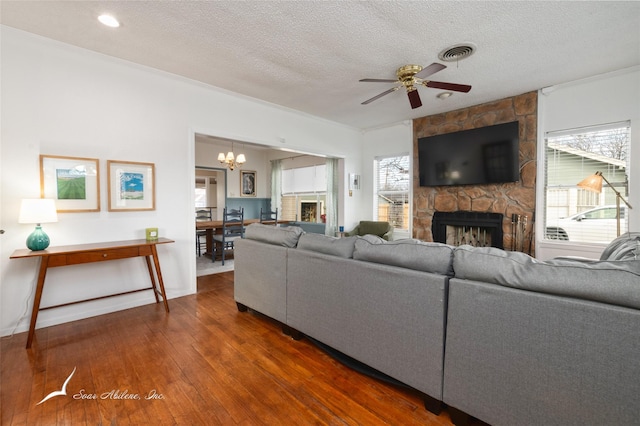 living room with a stone fireplace, dark hardwood / wood-style floors, crown molding, a textured ceiling, and ceiling fan with notable chandelier