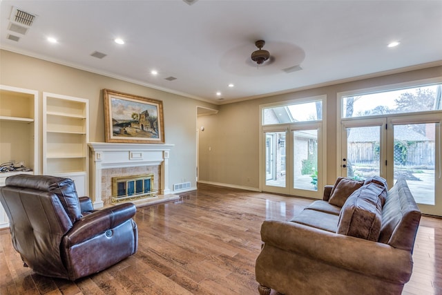 living room featuring light hardwood / wood-style flooring, built in features, ceiling fan, ornamental molding, and a tiled fireplace