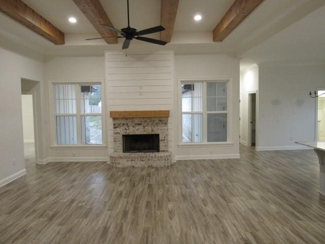 unfurnished living room with beamed ceiling, a wealth of natural light, a fireplace, and dark hardwood / wood-style flooring