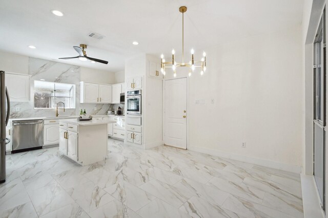 kitchen with white cabinetry, stainless steel appliances, a kitchen island, pendant lighting, and ceiling fan with notable chandelier