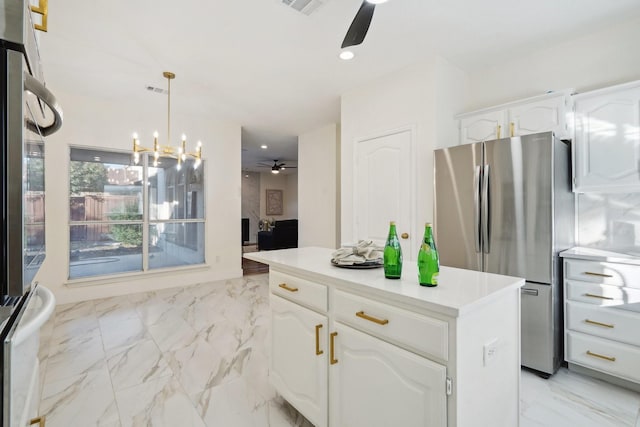 kitchen featuring stainless steel refrigerator, a kitchen island, pendant lighting, ceiling fan with notable chandelier, and white cabinets