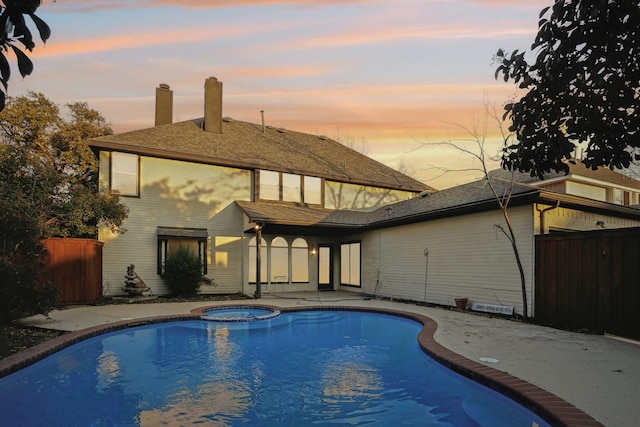 pool at dusk with a patio area and an in ground hot tub