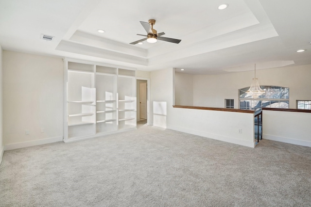 unfurnished living room with ceiling fan with notable chandelier, a tray ceiling, and carpet flooring