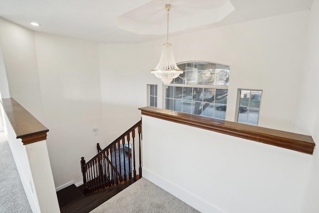 stairs featuring a raised ceiling and a notable chandelier