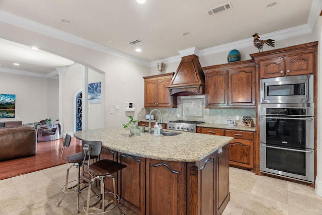 kitchen with a kitchen island with sink, sink, decorative backsplash, custom range hood, and stainless steel appliances