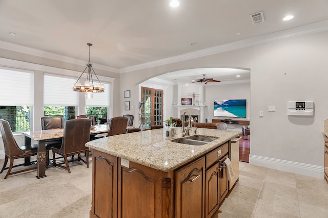 kitchen with light stone countertops, sink, decorative light fixtures, a center island with sink, and ceiling fan with notable chandelier