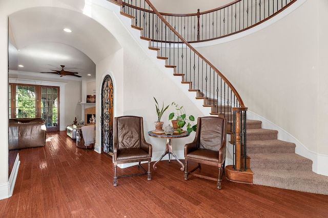 interior space with arched walkways, a fireplace, stairway, a ceiling fan, and hardwood / wood-style floors