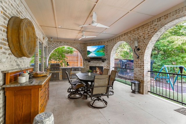 view of patio / terrace featuring an outdoor kitchen, area for grilling, a brick fireplace, ceiling fan, and a playground