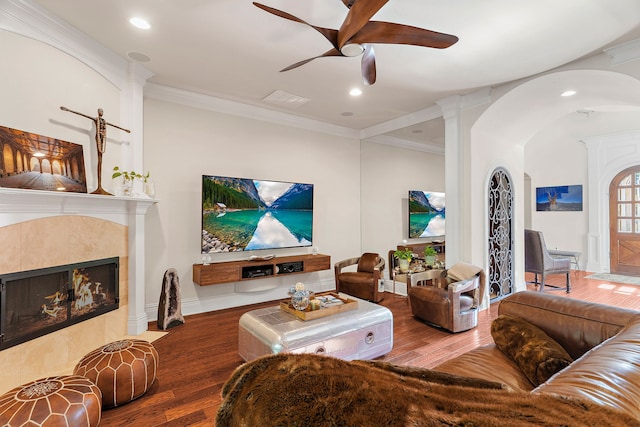 living room with ceiling fan, wood-type flooring, crown molding, and a tile fireplace