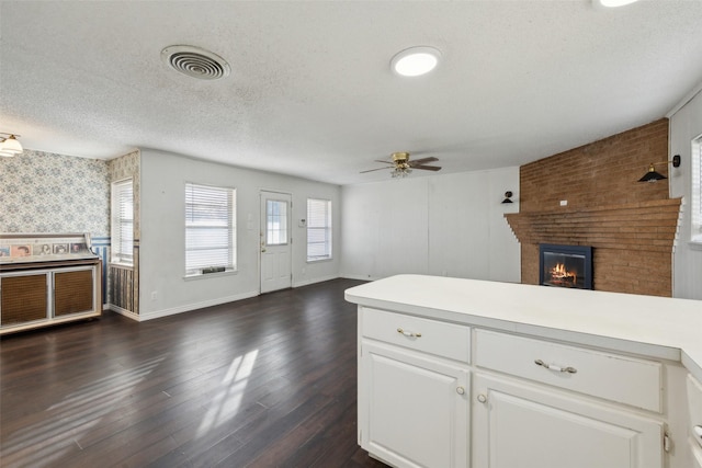 kitchen featuring white cabinetry, ceiling fan, dark hardwood / wood-style flooring, a textured ceiling, and a fireplace