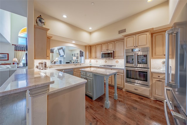 kitchen featuring kitchen peninsula, stainless steel appliances, a kitchen island, light stone counters, and a breakfast bar