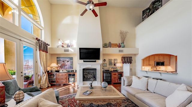 living room with ceiling fan, wine cooler, hardwood / wood-style floors, a towering ceiling, and french doors