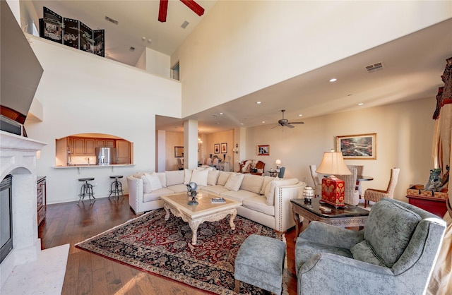 living room with ceiling fan, a high end fireplace, dark hardwood / wood-style flooring, and a towering ceiling