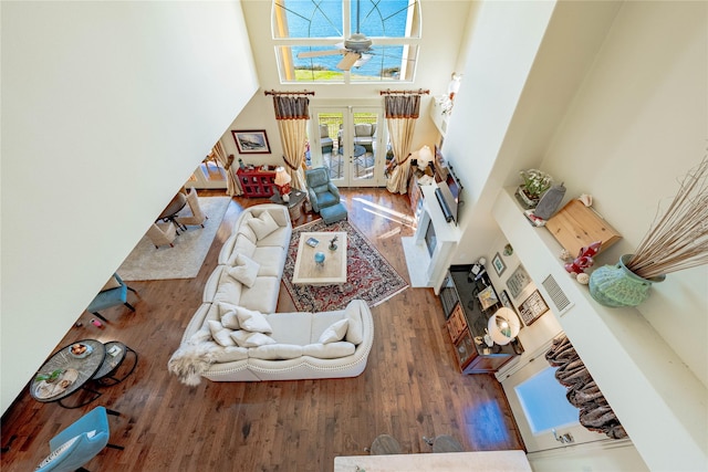 living room with ceiling fan, a high ceiling, hardwood / wood-style floors, and french doors