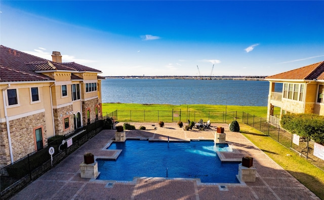 view of swimming pool featuring pool water feature, a lawn, and a water view