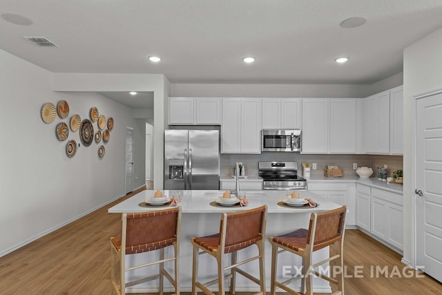 kitchen with a breakfast bar, tasteful backsplash, a center island with sink, stainless steel appliances, and white cabinets