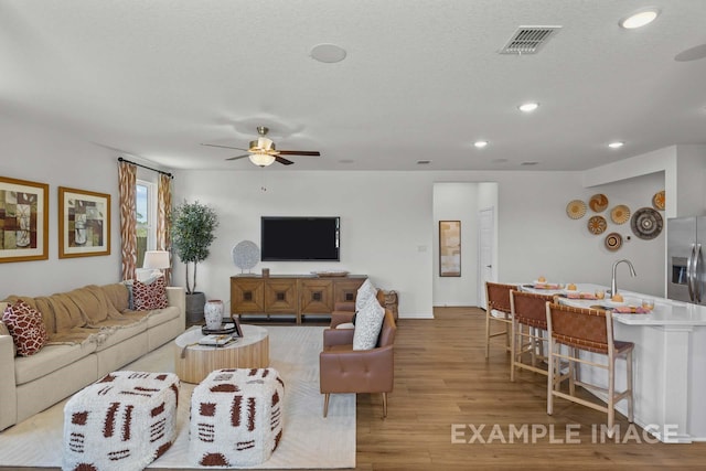 living room with ceiling fan, a textured ceiling, and light hardwood / wood-style flooring