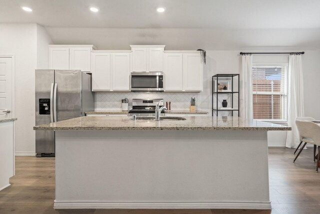 kitchen featuring white cabinets, a center island with sink, light stone counters, and appliances with stainless steel finishes