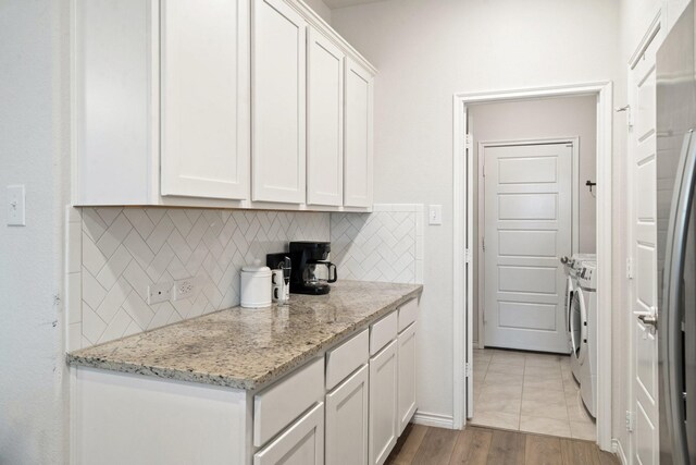 kitchen with light stone countertops, light hardwood / wood-style flooring, independent washer and dryer, decorative backsplash, and white cabinets