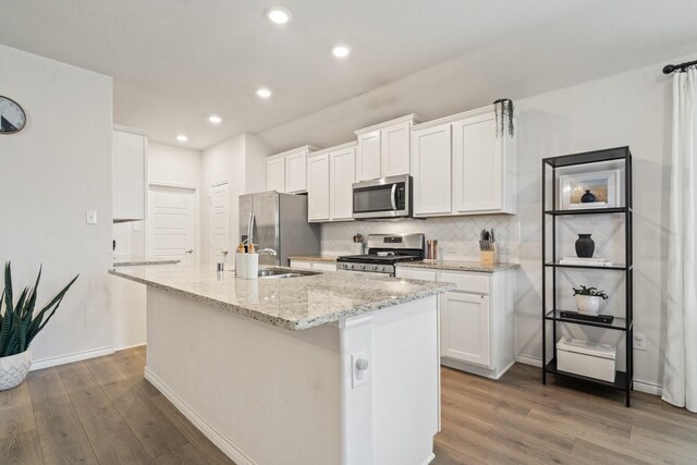 kitchen with white cabinets, appliances with stainless steel finishes, light stone countertops, and an island with sink