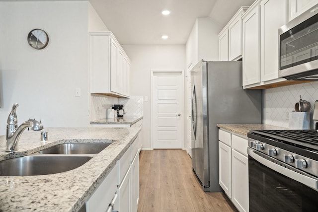 kitchen featuring appliances with stainless steel finishes, light wood-type flooring, light stone counters, sink, and white cabinets