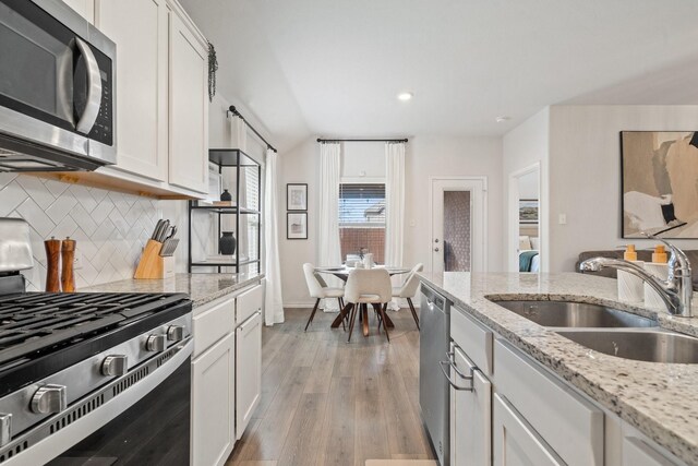 kitchen featuring decorative backsplash, appliances with stainless steel finishes, light stone counters, sink, and white cabinetry