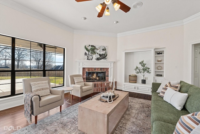 living room with dark wood-type flooring, ceiling fan, crown molding, and a brick fireplace