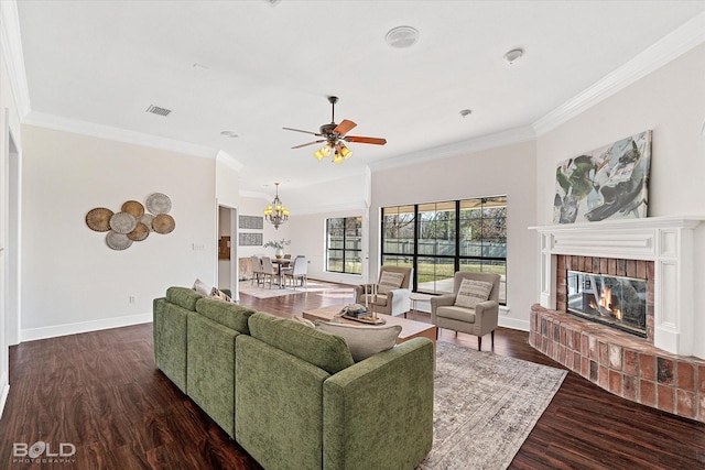 living room featuring a brick fireplace, crown molding, dark wood-type flooring, and ceiling fan with notable chandelier