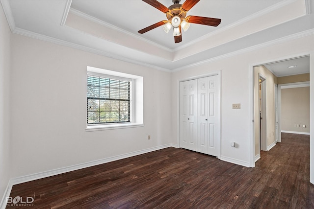 unfurnished bedroom featuring dark hardwood / wood-style flooring, ceiling fan, a tray ceiling, crown molding, and a closet