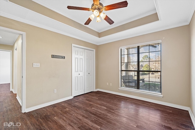 unfurnished bedroom featuring ceiling fan, ornamental molding, a raised ceiling, dark hardwood / wood-style flooring, and a closet