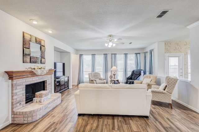 living room featuring a textured ceiling, ceiling fan, light hardwood / wood-style flooring, and a brick fireplace