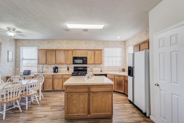 kitchen with black appliances, ceiling fan, light wood-type flooring, a textured ceiling, and a kitchen island