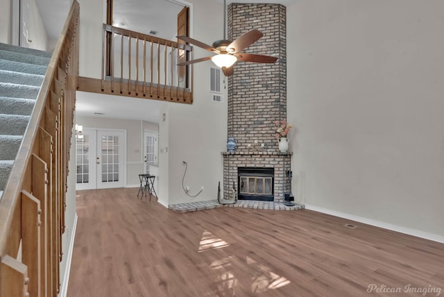 unfurnished living room with high vaulted ceiling, french doors, a brick fireplace, ceiling fan, and light hardwood / wood-style floors