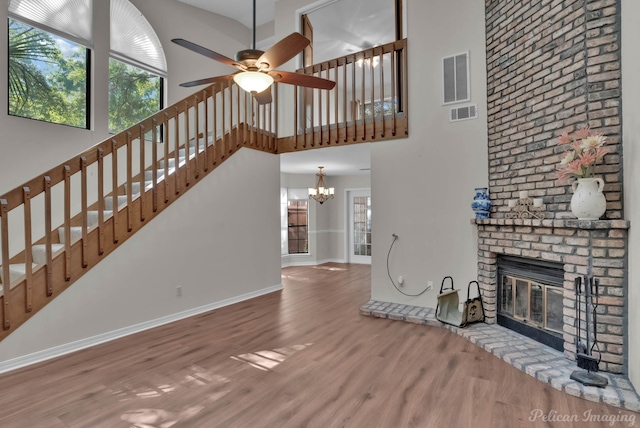 unfurnished living room featuring a fireplace, ceiling fan with notable chandelier, wood-type flooring, and a high ceiling