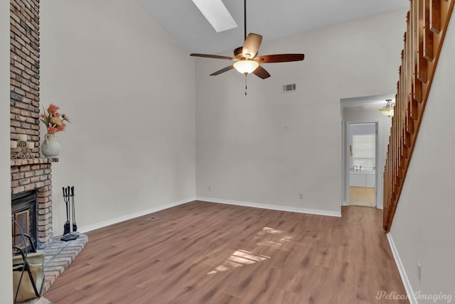 unfurnished living room with ceiling fan, light hardwood / wood-style flooring, a fireplace, and a skylight