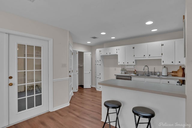 kitchen with sink, a breakfast bar area, light hardwood / wood-style flooring, kitchen peninsula, and white cabinets