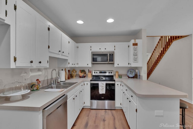 kitchen with appliances with stainless steel finishes, white cabinetry, sink, kitchen peninsula, and light wood-type flooring