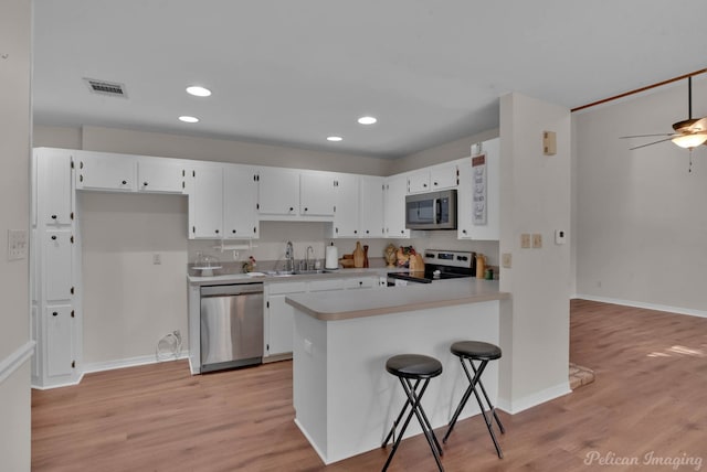 kitchen featuring appliances with stainless steel finishes, a breakfast bar area, white cabinets, light hardwood / wood-style floors, and kitchen peninsula