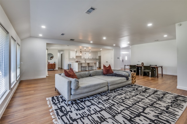 living room featuring light hardwood / wood-style floors, lofted ceiling, and sink