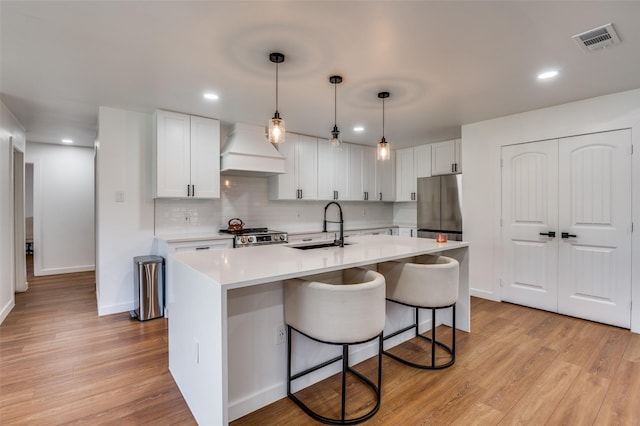 kitchen with white cabinetry, sink, hanging light fixtures, and custom range hood