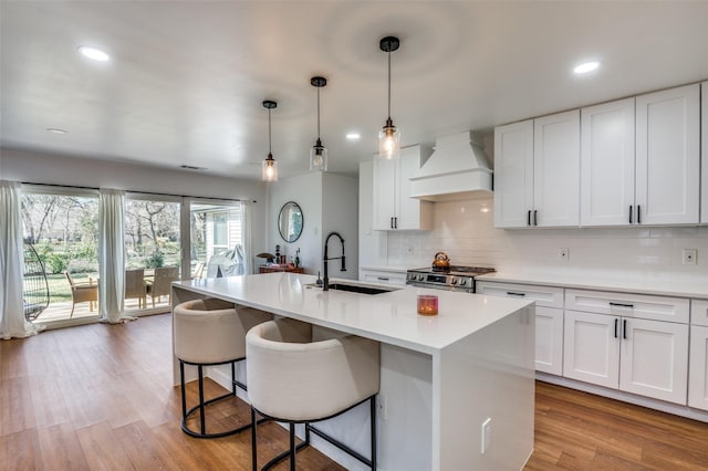 kitchen featuring an island with sink, premium range hood, white cabinetry, and sink