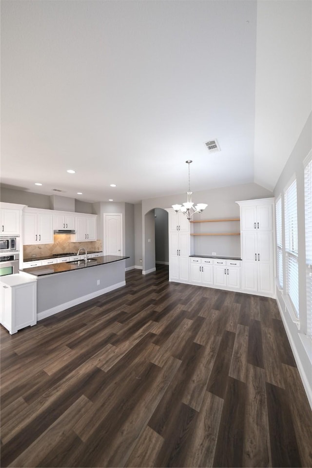 unfurnished living room with dark wood-style floors, visible vents, arched walkways, a sink, and vaulted ceiling