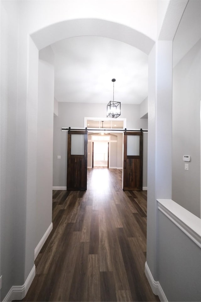 corridor featuring dark wood finished floors, arched walkways, baseboards, and a barn door