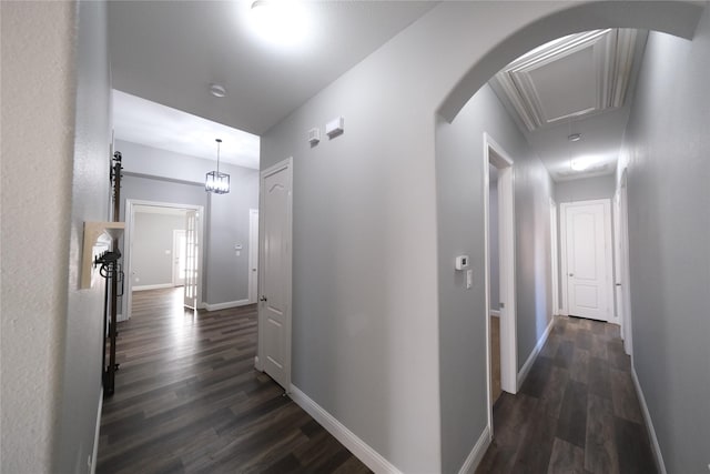 hall with arched walkways, attic access, dark wood-type flooring, and baseboards