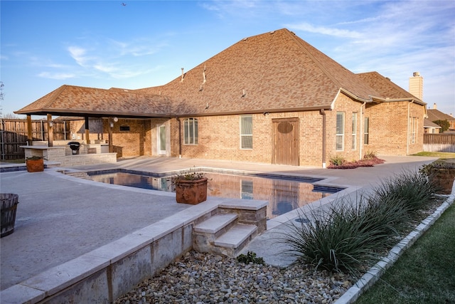 rear view of house featuring brick siding, a shingled roof, a patio, and fence